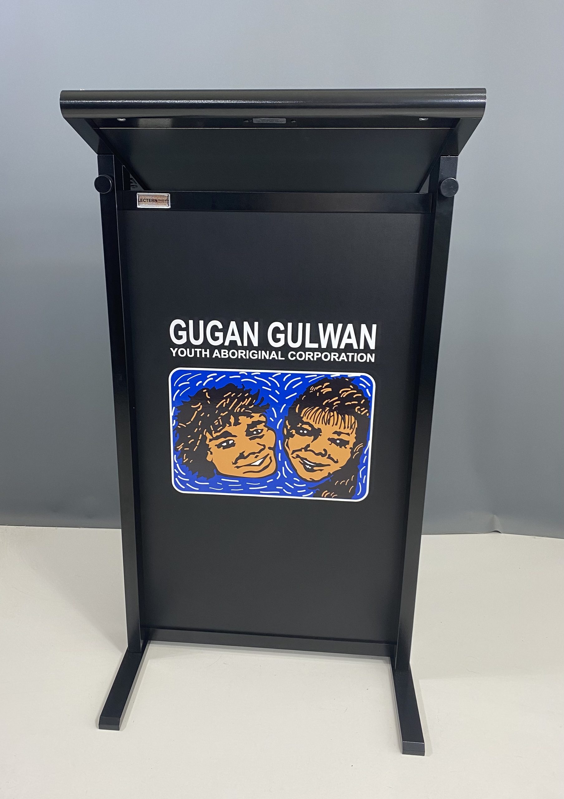 Black lectern with “Gugan Gulwan Youth Aboriginal Corporation” logo on the front