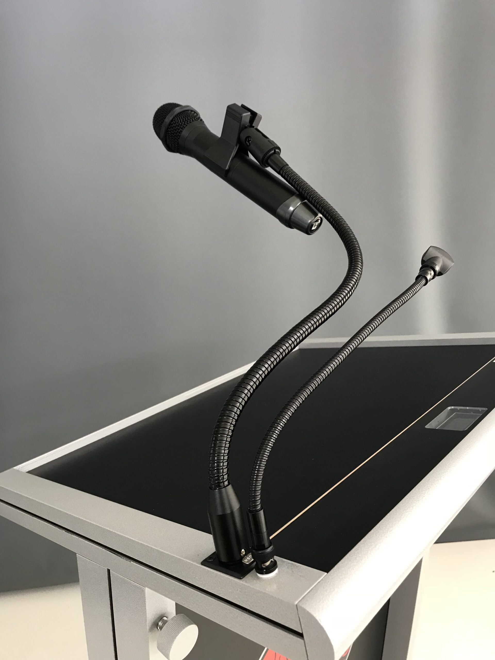 Flexible gooseneck microphone holder attached to a lectern, designed to securely hold handheld microphones for presentations and public speaking.